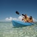 Two young women paddle in a kayak in shallow ocean water